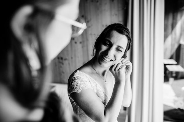 Braut beim Anlegen der Ohrringe vor der Hochzeit auf der Gutsalm Harlachberg