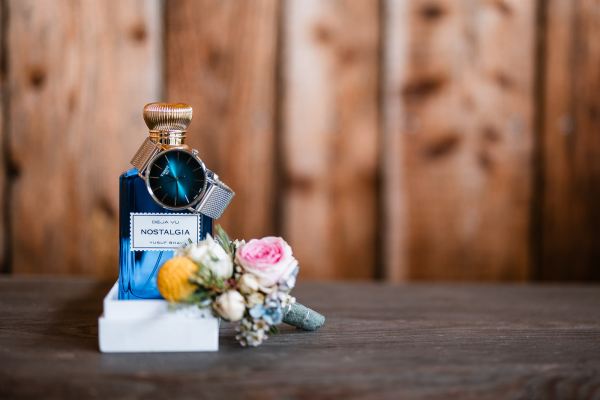 Detailaufnahme: Parfüm, Uhr und Hochzeitsanstecker bei der Hochzeit auf der Gutsalm Harlachberg