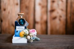 Detailaufnahme: Parfüm, Uhr und Hochzeitsanstecker bei der Hochzeit auf der Gutsalm Harlachberg