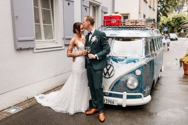 Brautpaar küsst sich vor VW-Bus am Hochzeitstag
