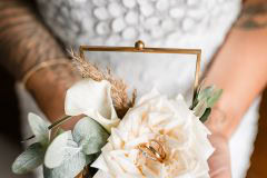 Braut hält Eheringe in Glasbox mit Rose beim Getting Ready